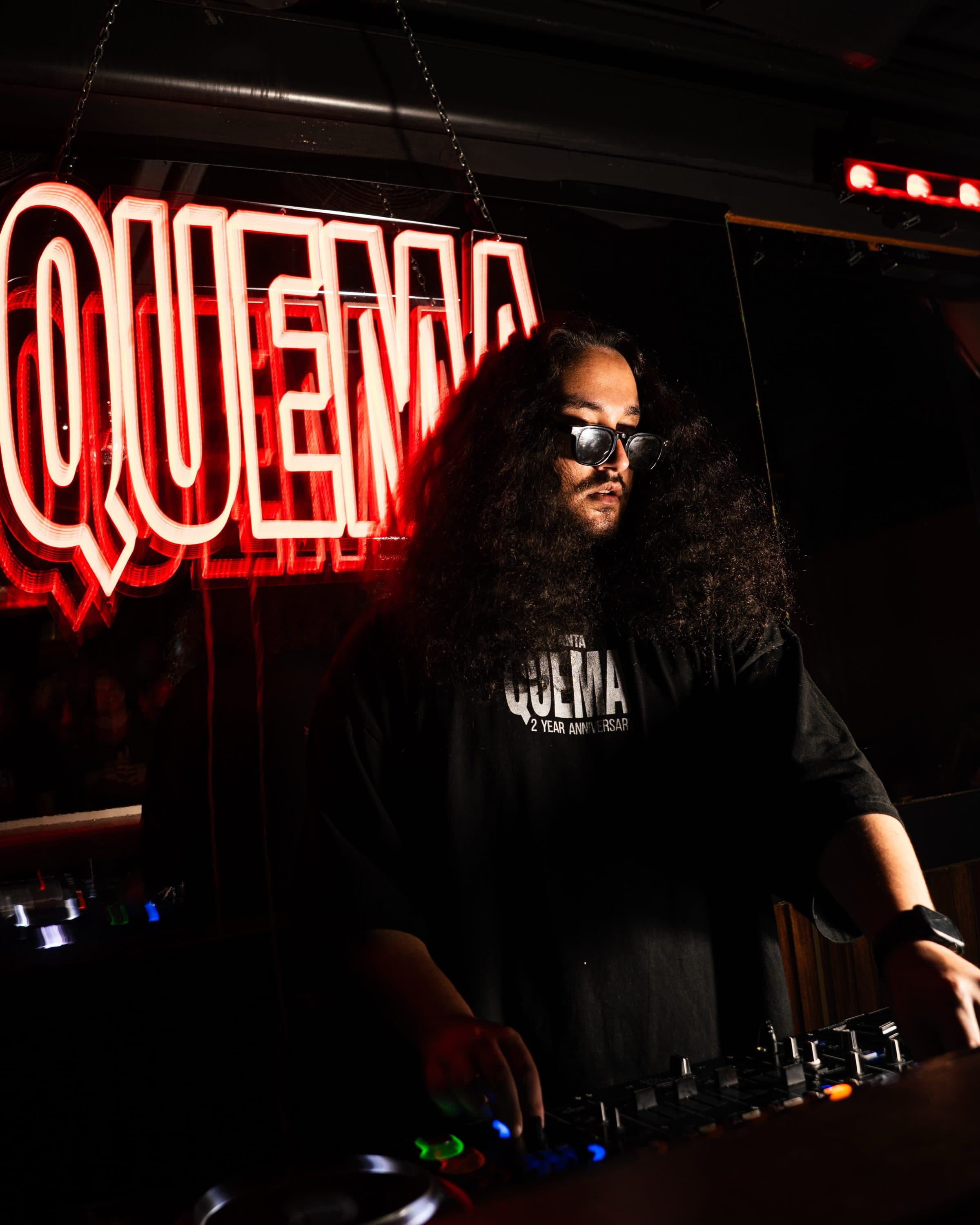 ANÜ at the decks in the QUEMA 2 Year Anniversary tee, under the QUEMA neon