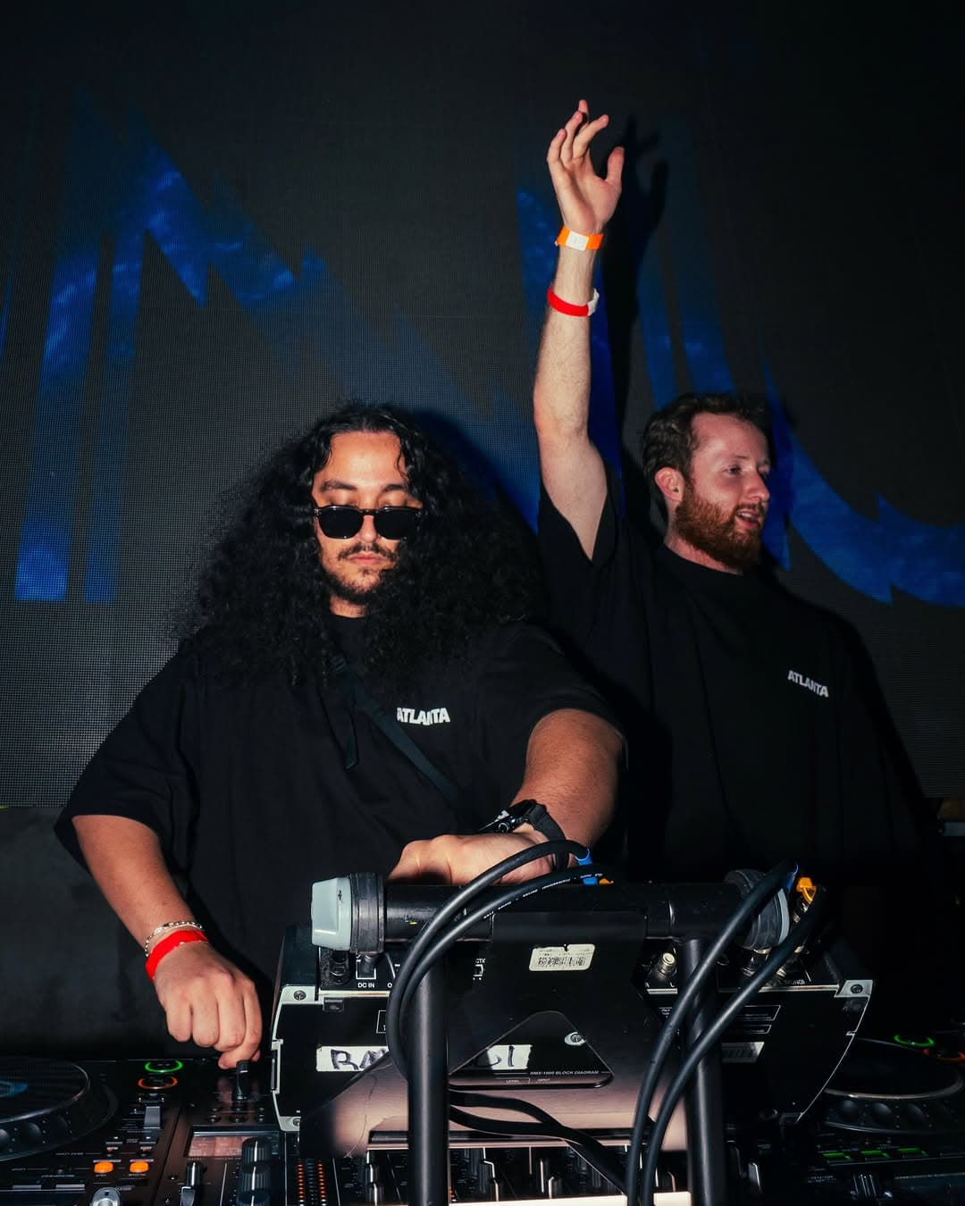 Two DJs at the decks, one with an arm raised